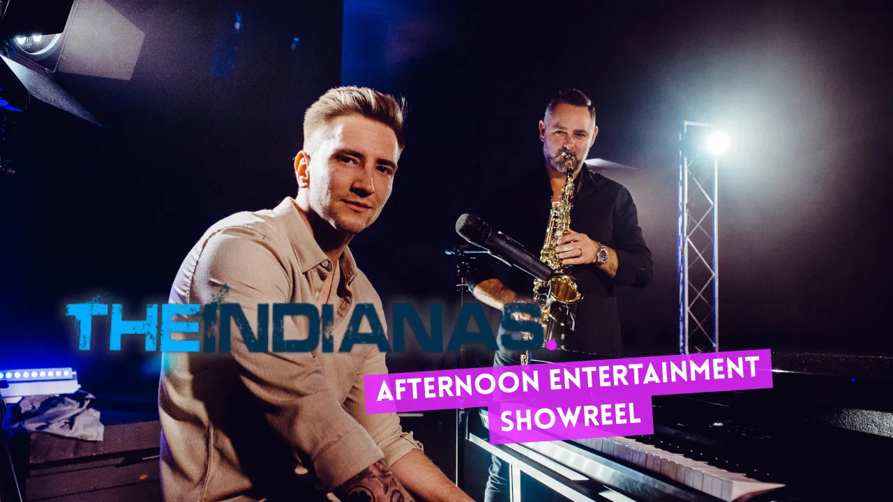 Man sitting at a piano looking at the camera while another man plays saxophone in a dimly lit studio with text 'THE INDIANAS' and 'AFTERNOON ENTERTAINMENT SHOWREEL'.
